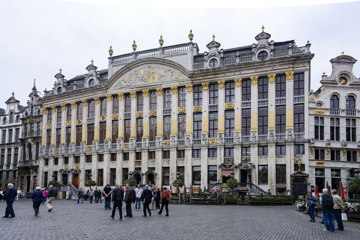 Ornate guild houses with gilded details on the Grand-Place in Brussels, with people crossing the square