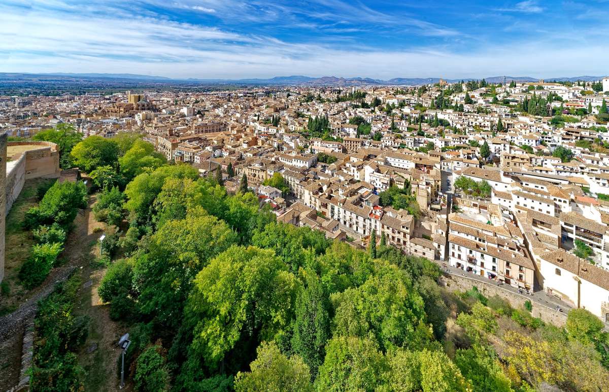 Whitewashed houses and rooftops of Granada seen from the Alhambra, with trees on the hillside below