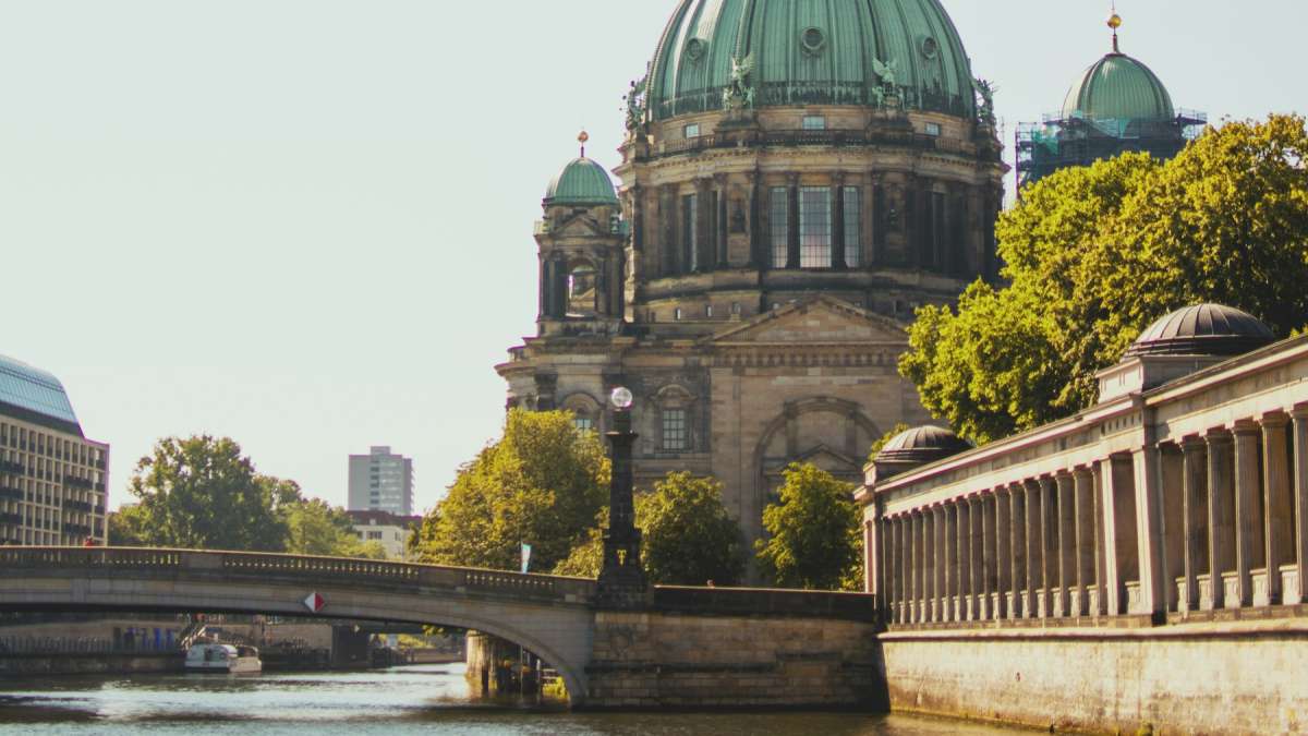 Berlin Cathedral's green copper dome beside a stone bridge and colonnade on the Spree in warm sunlight