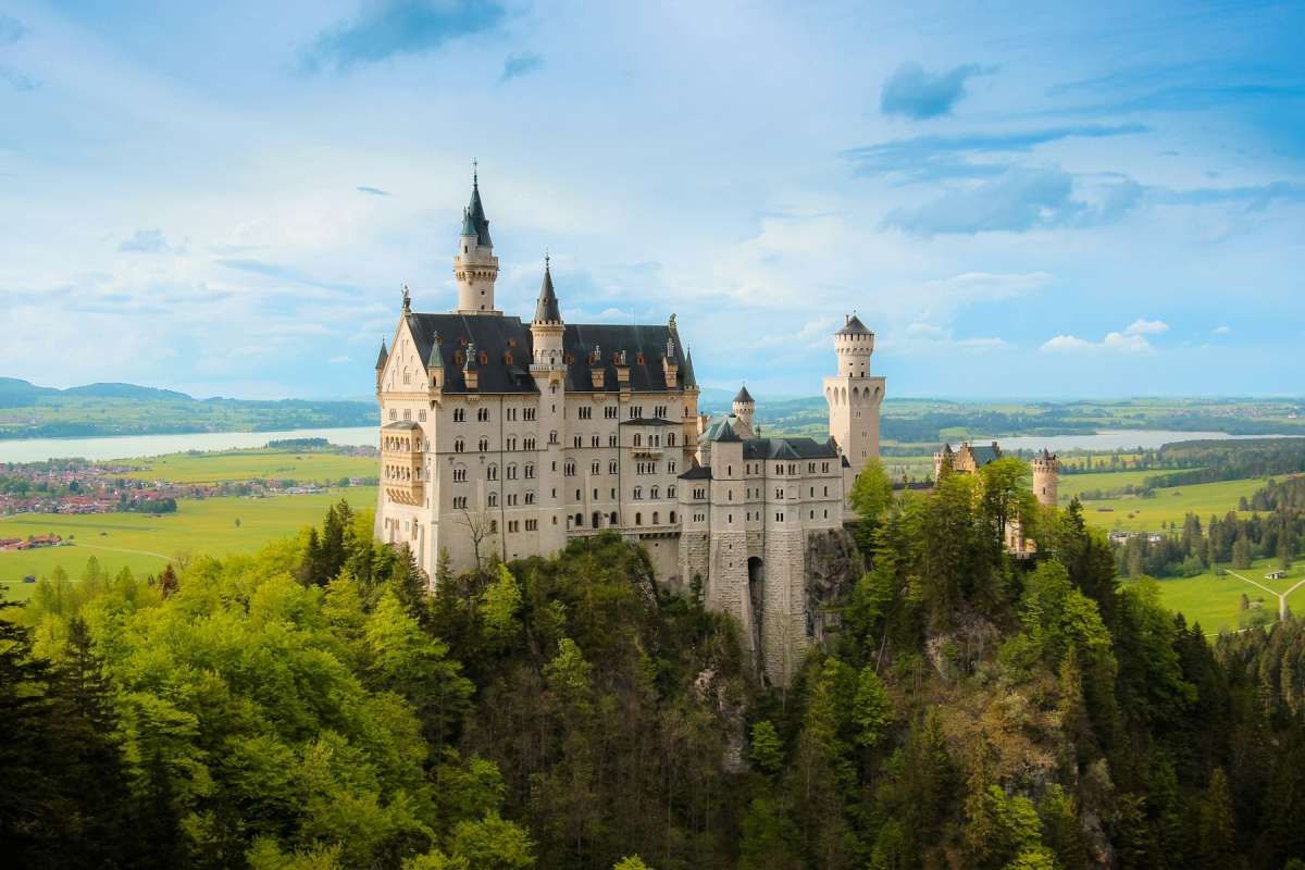 Neuschwanstein Castle on a wooded hilltop above green Bavarian countryside under a blue sky